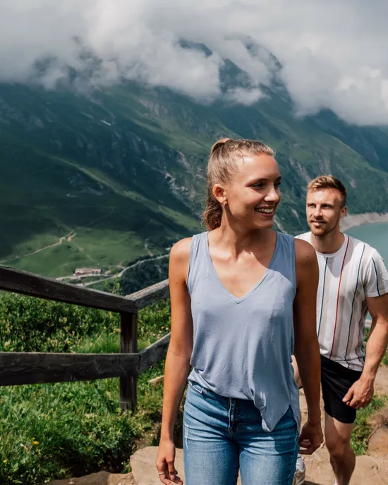 Coppia che fa escursione su sentiero di montagna con lago alpino e paesaggio estivo